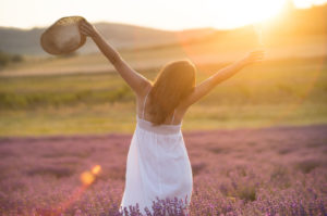 55267568 - beautiful young woman with a white dress and a straw hat standing in the middle of a lavender field at in the golden light of the sunset praising the beauty of life.